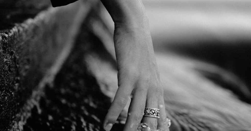 A woman's hand delicately touches flowing water, capturing tranquility and reflection in black and white.
